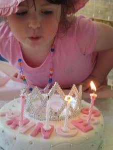 blowing out four year old's birthday candles on princess tiara cake